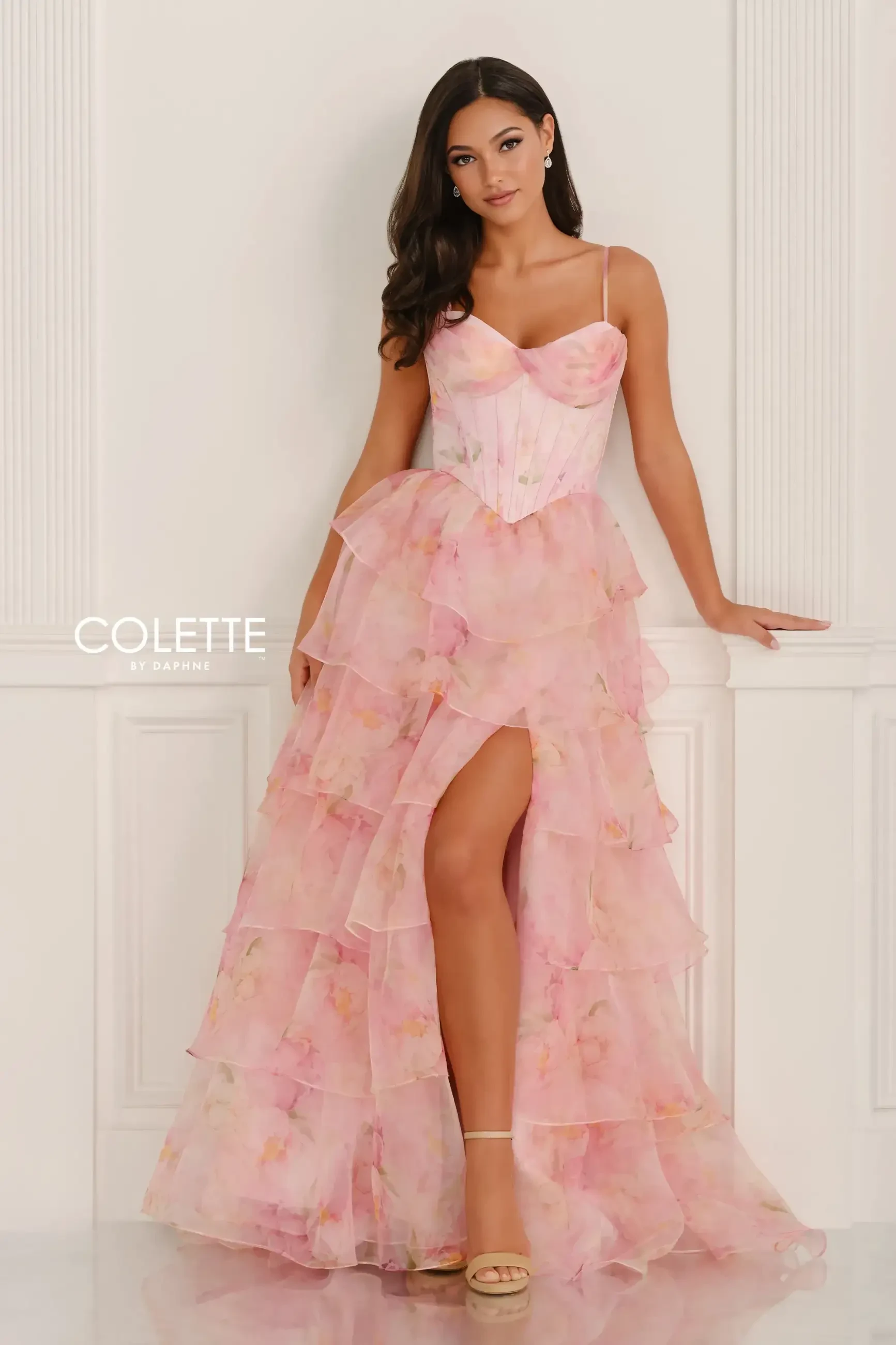 A model wearing a pink, layered gown with a thigh-high slit, posing elegantly against a neutral background.