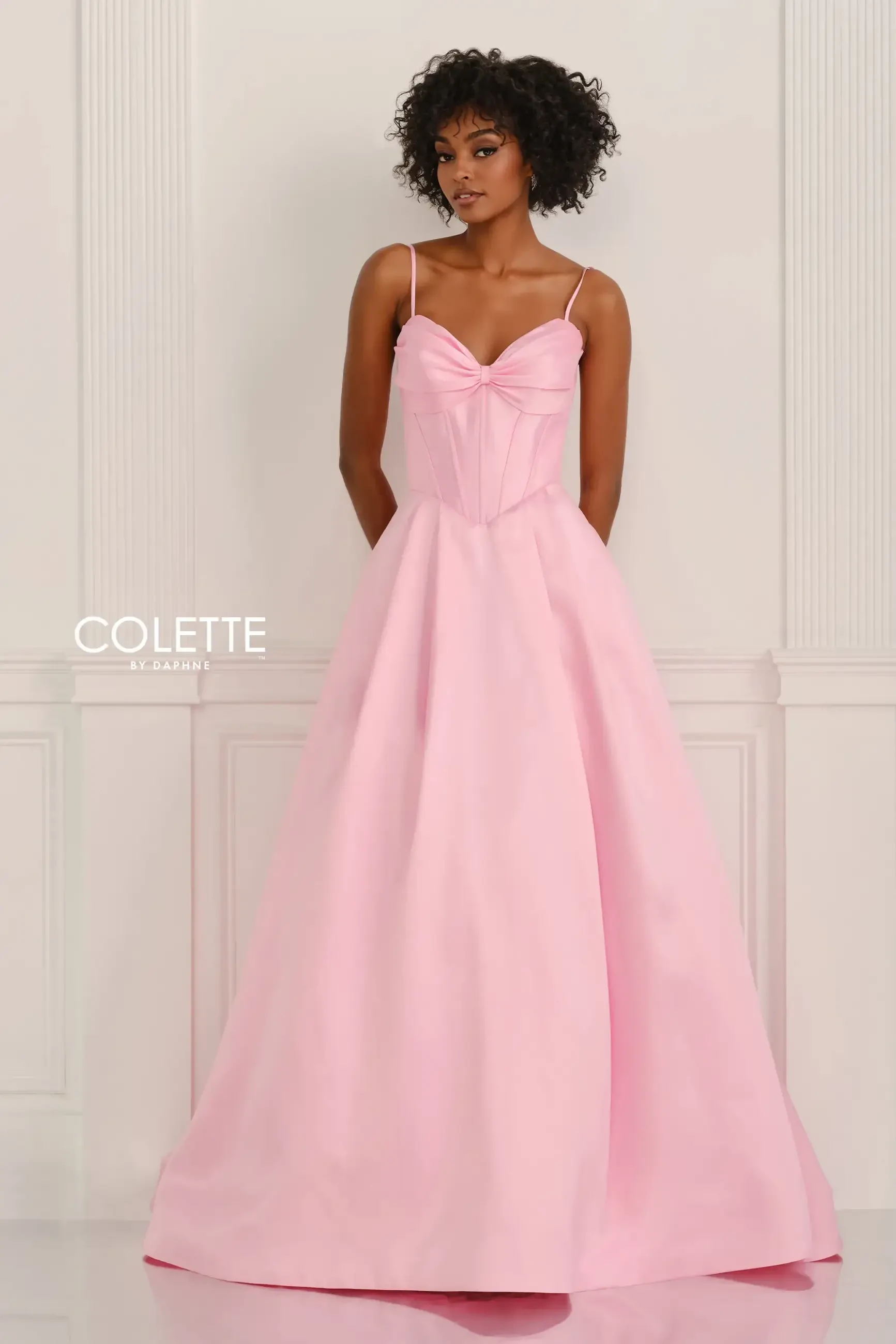 A model wearing a pink gown with thin straps, standing against a white background.
