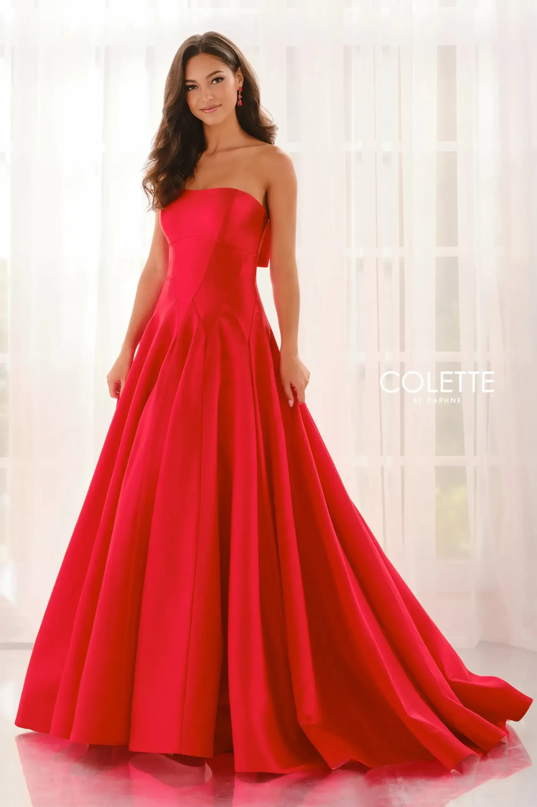 model is wearing a strapless red ball gown prom dress with a bow on the back