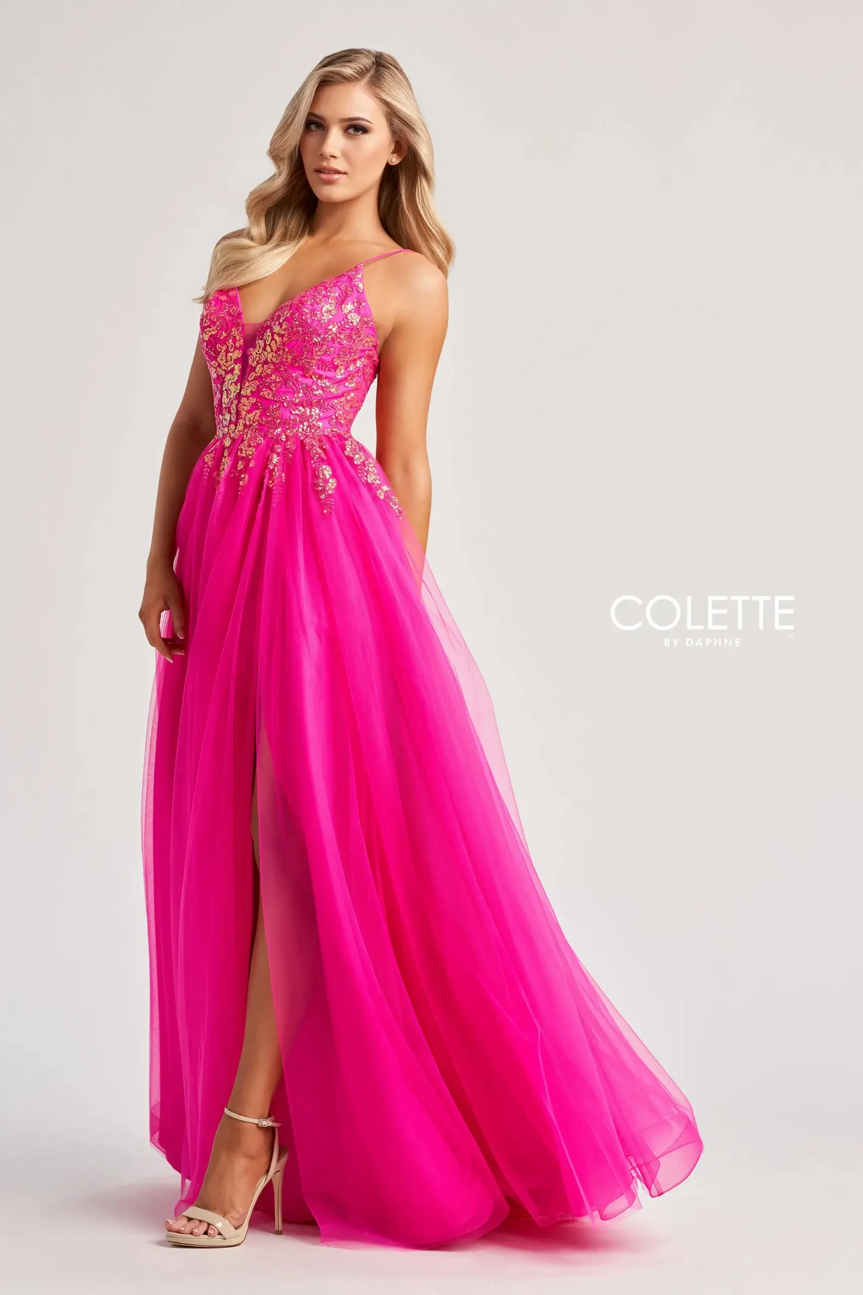 model is wearing a sleeveless hot pink evening gown with a tulle skirt, spaghetti straps, and a high slit