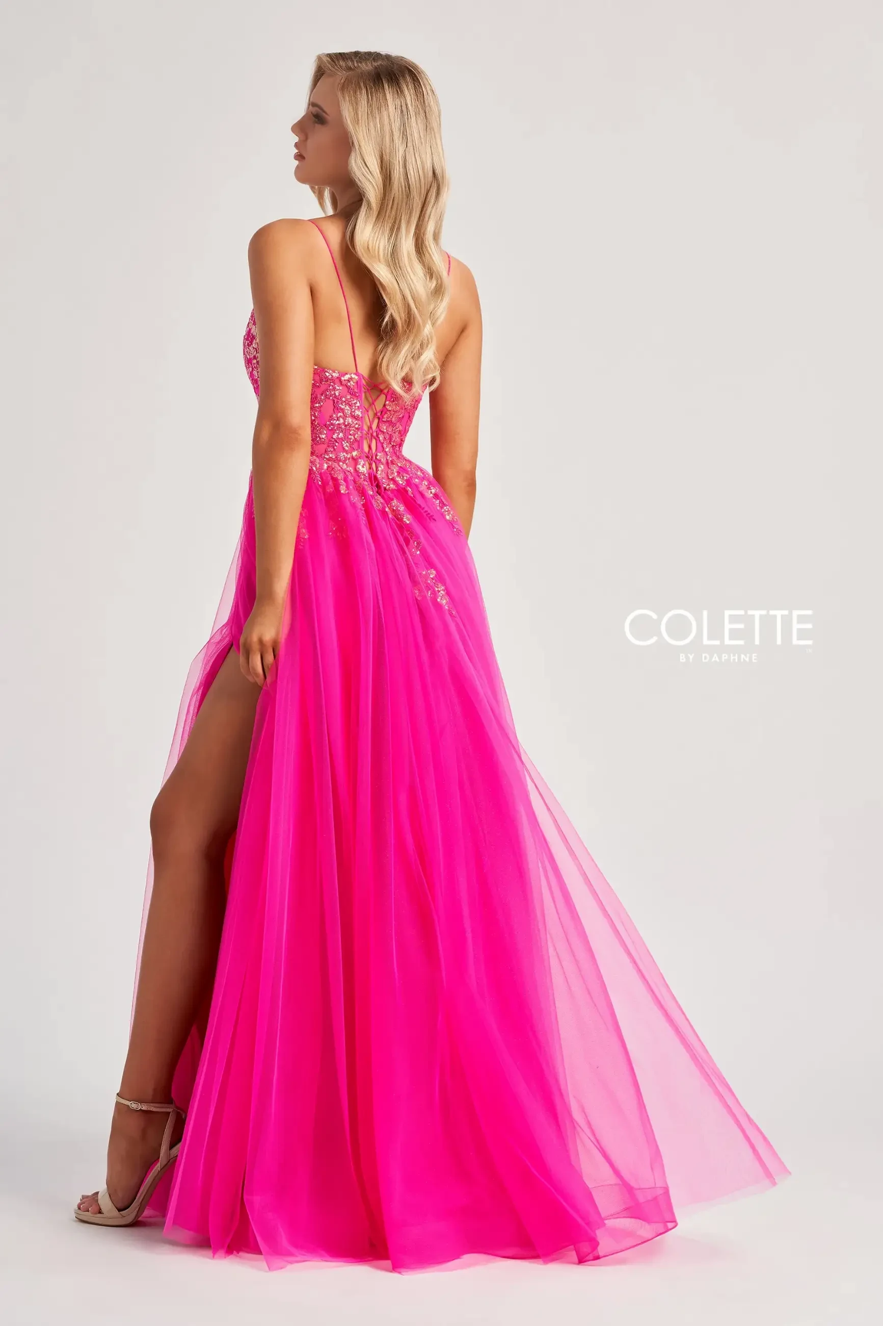 model is wearing a sleeveless hot pink evening gown with a tulle skirt, spaghetti straps, and a high slit