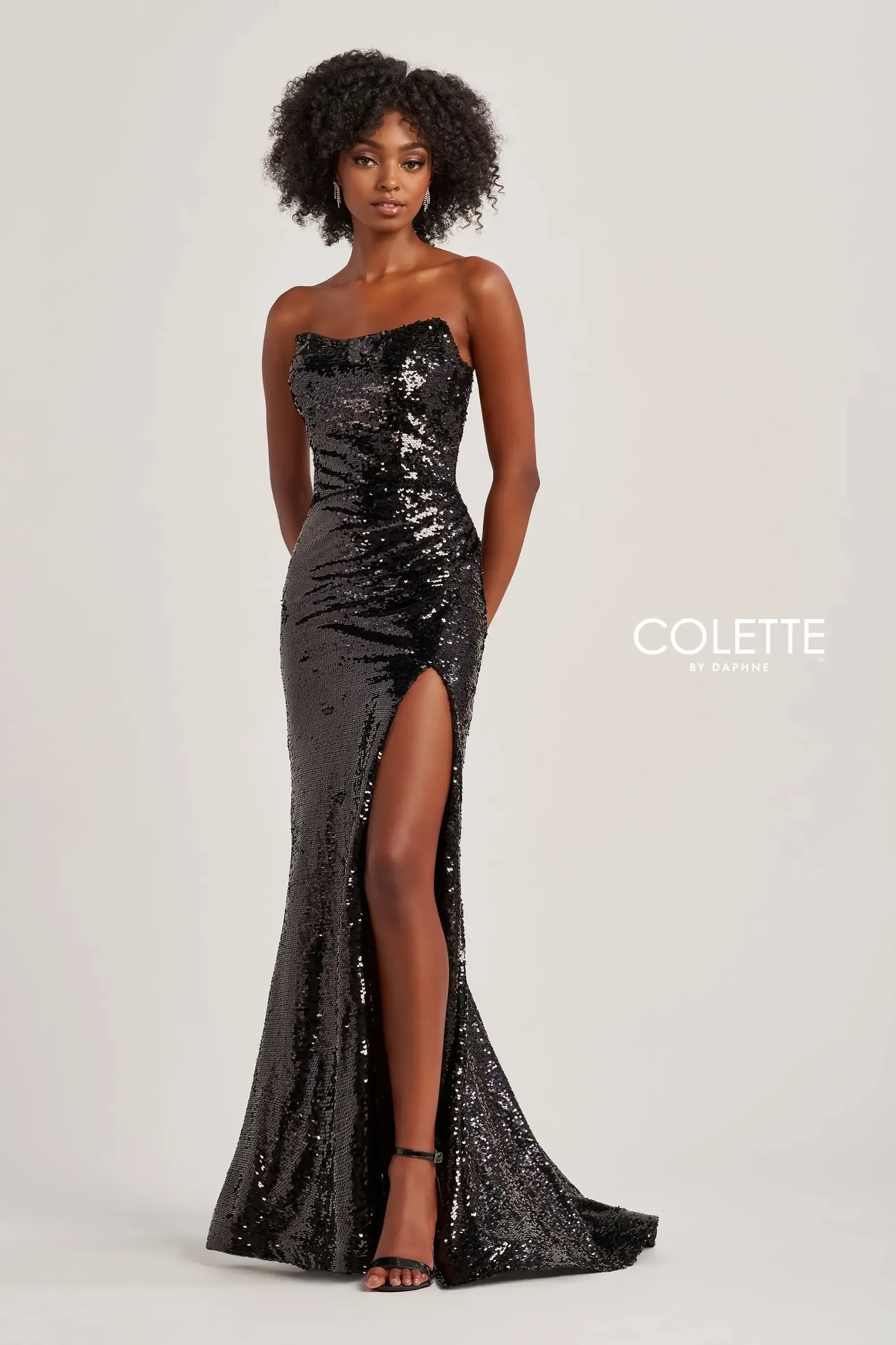 Model is wearing a sheath evening dress in black with a side slit and sheath silhouette