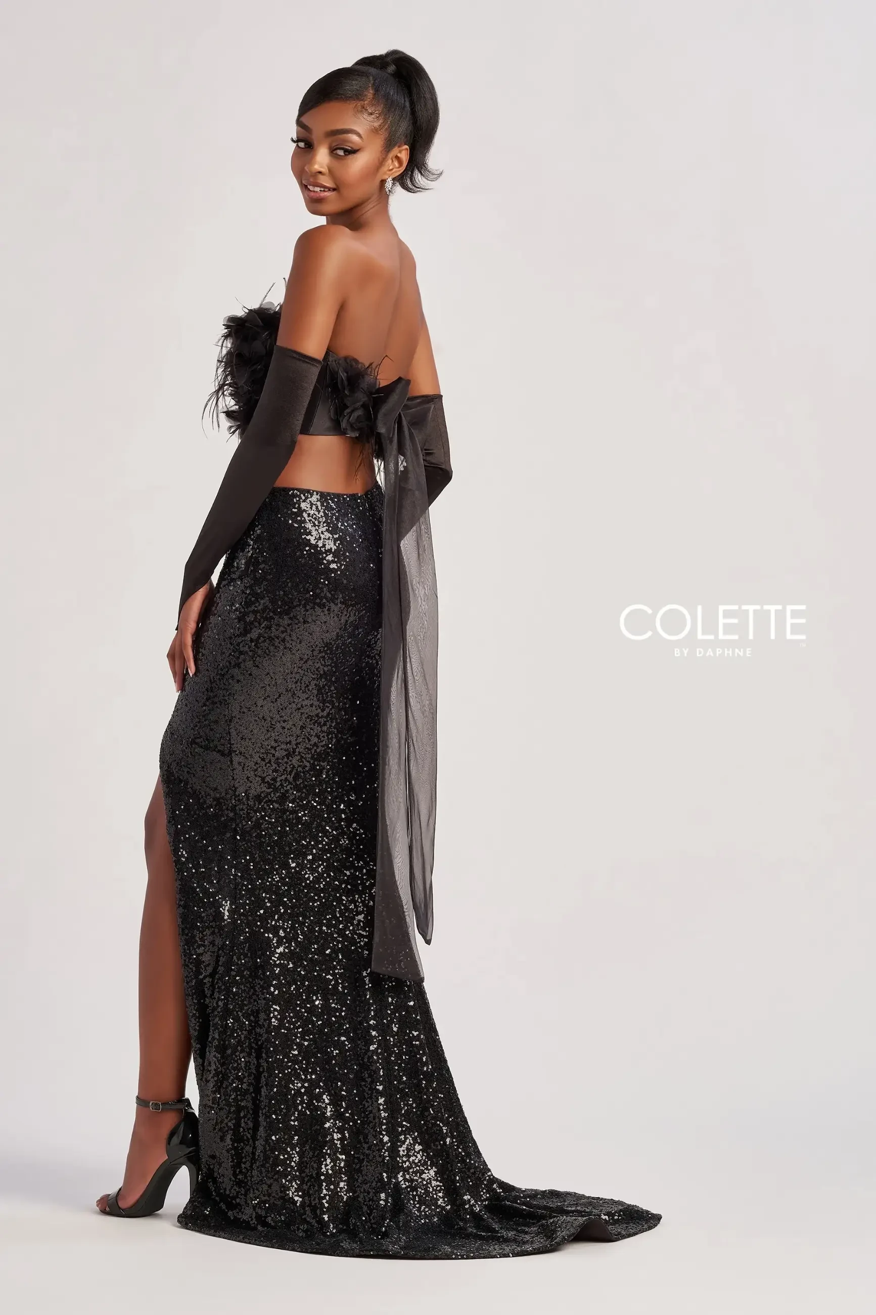 model is wearing a sleek black two piece prom dress with feathers