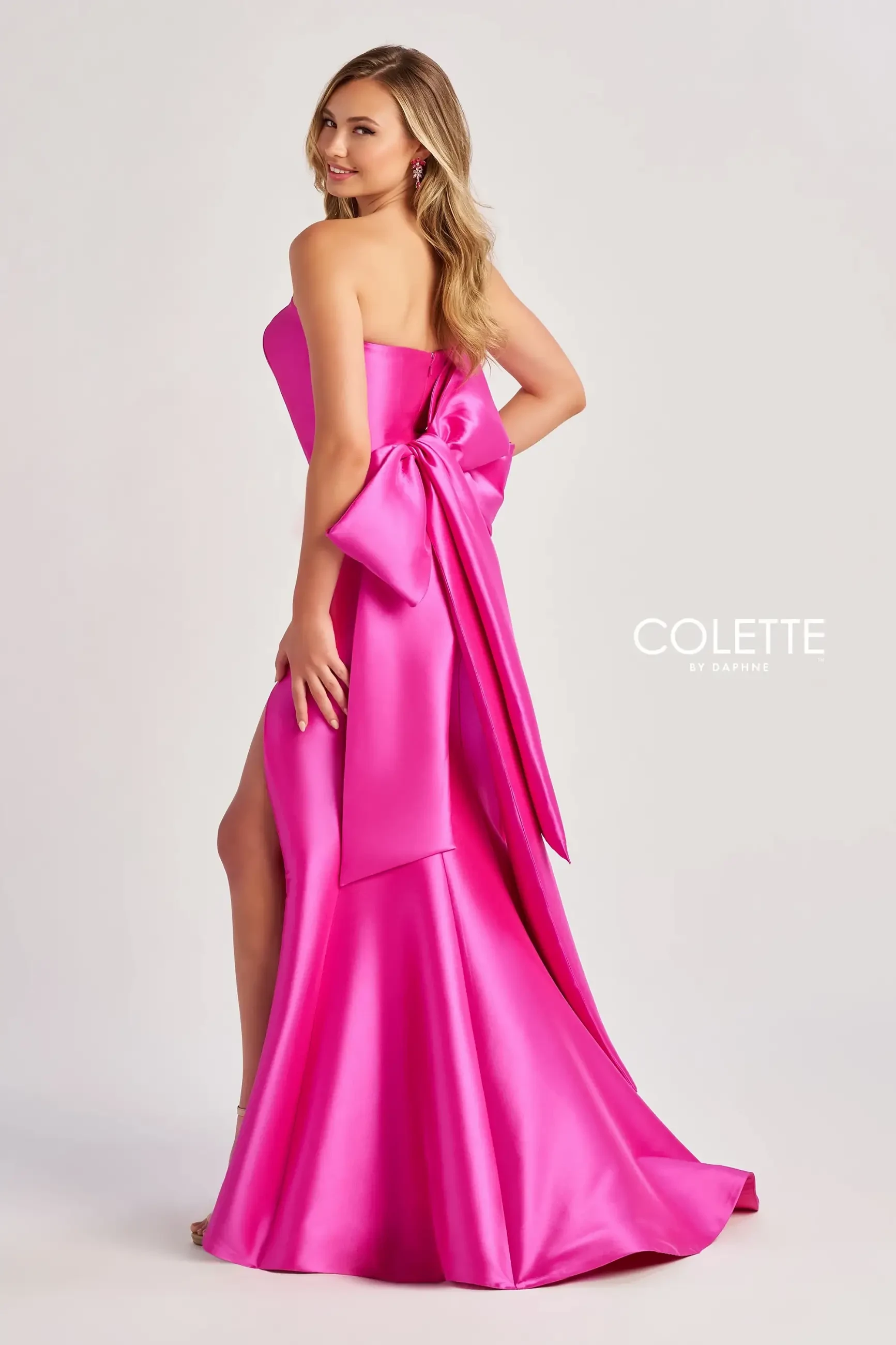 model is wearing a strapless hot pink evening gown with a huge bow on the back