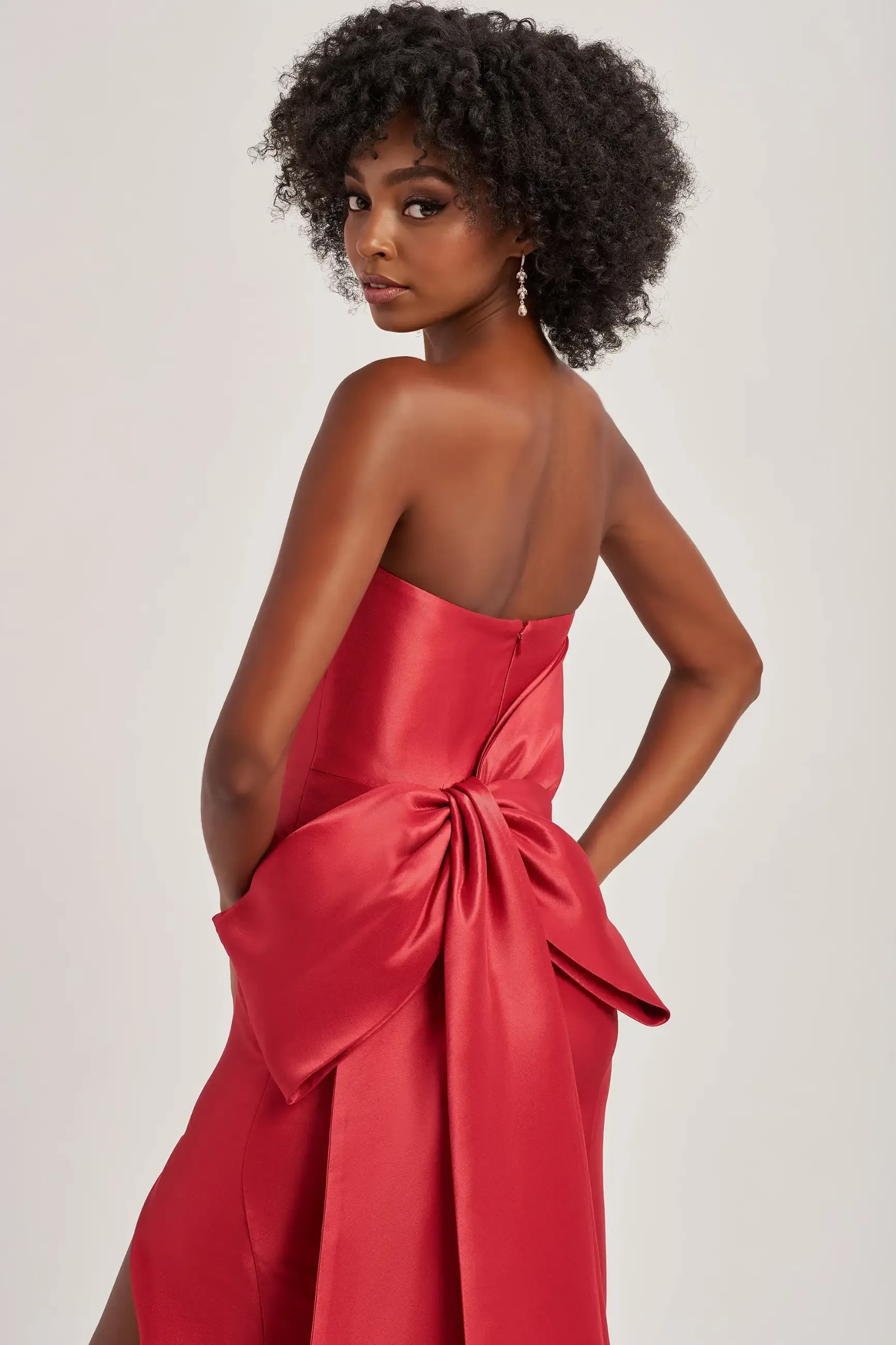 model is wearing a red strapless prom dress with a bow on the back
